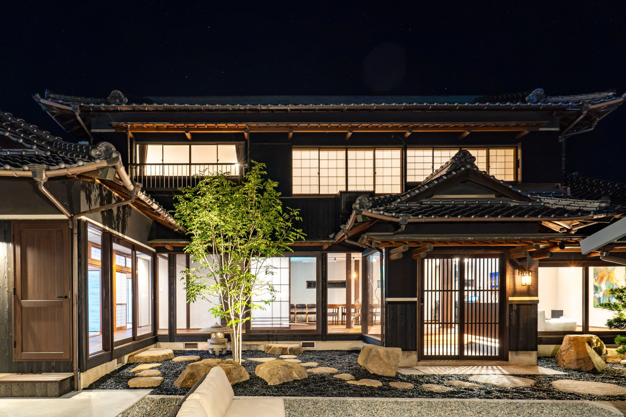 夜、窓に灯りのともったSumuの外観と石庭