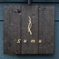 焼杉の板に金文字で記された「Sumu」の館銘